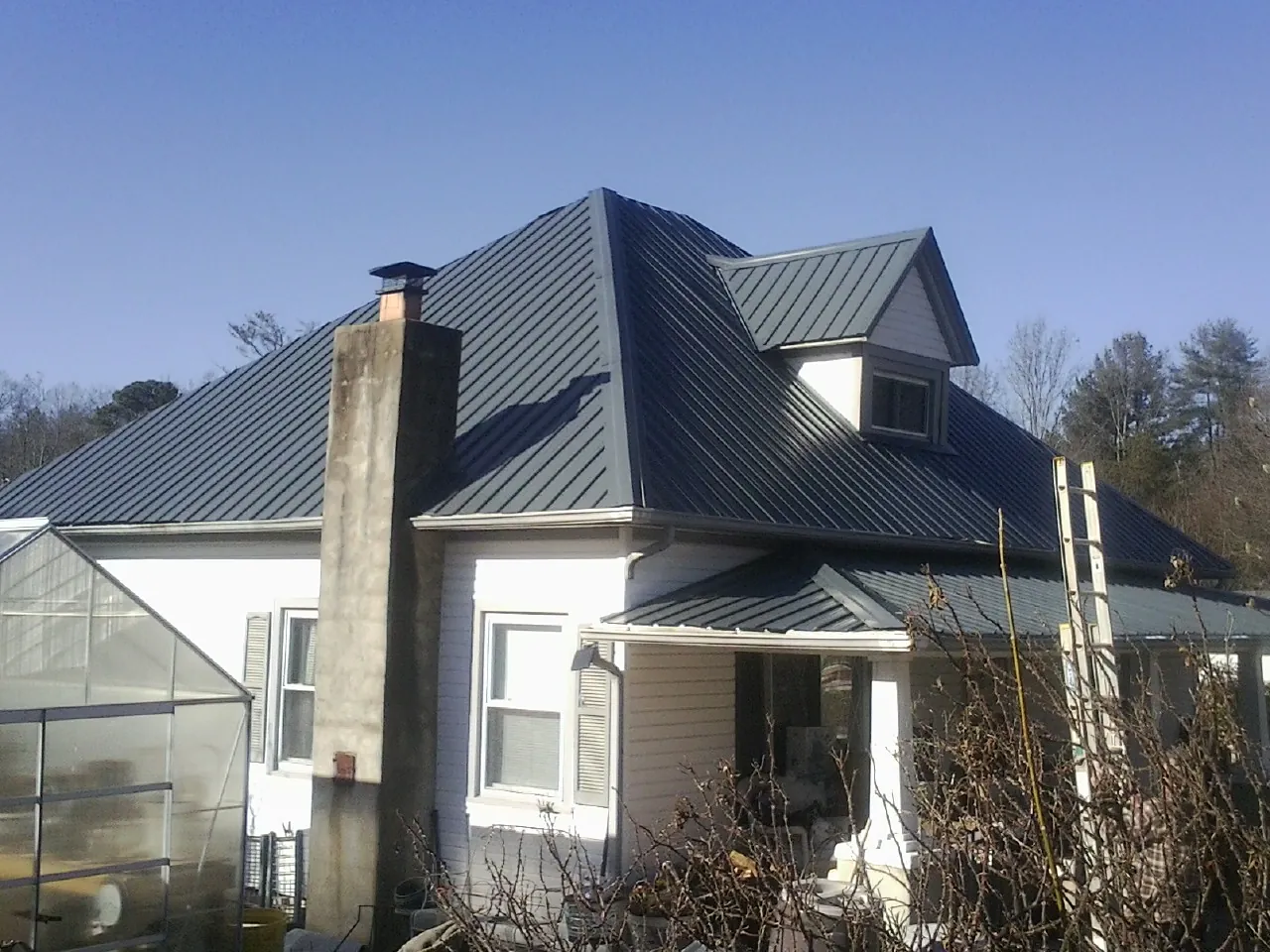 Dark blue standing seam metal roof on a white farmhouse with dormer — Slate & Tile Roof Repair by Roofing Brothers in Elberon
