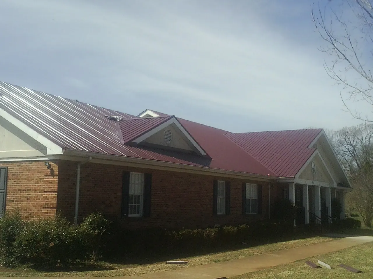 Red metal roof with gabled entries on a long brick building, from a Hail Damage Roof Repair job in Elberon