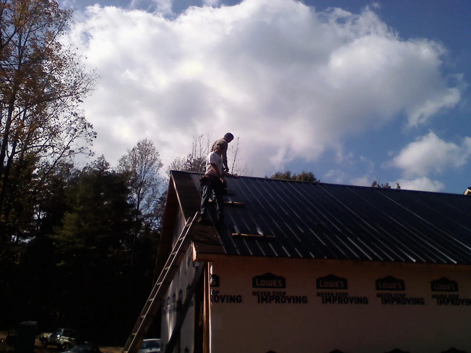 Roofer fastening dark metal panels high against a cloudy sky, from a Roof Inspection job in Elberon